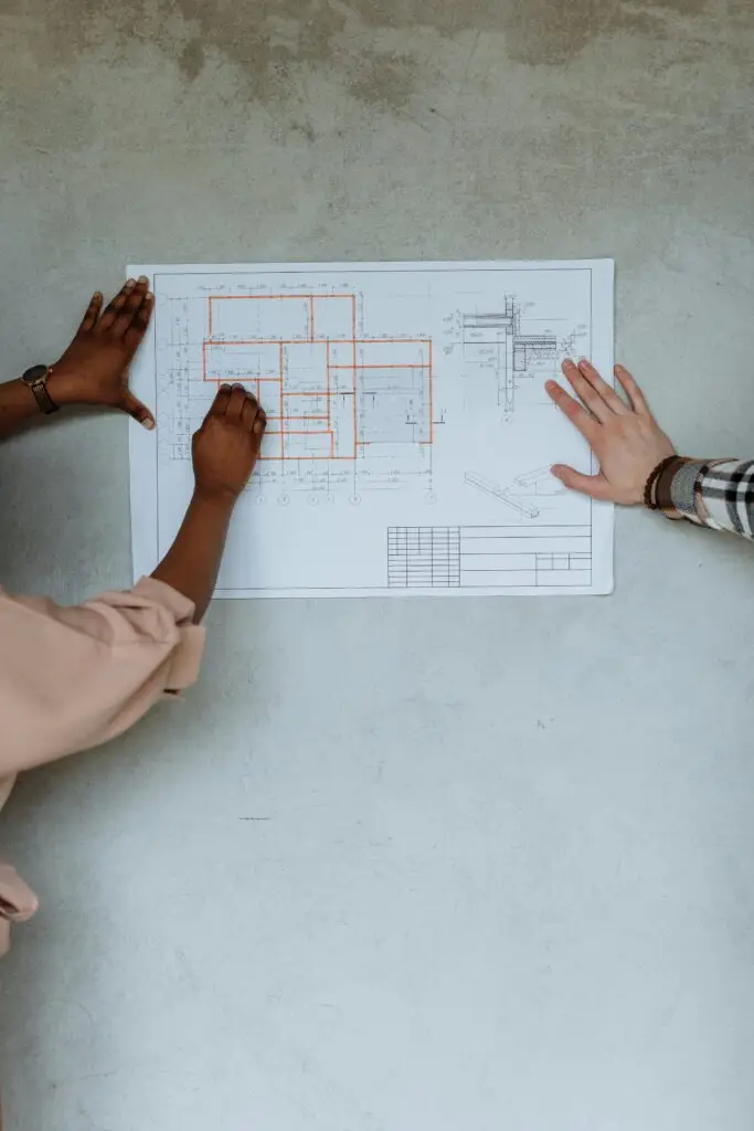 Two people collaborate on a blueprint plan in an indoor setting.